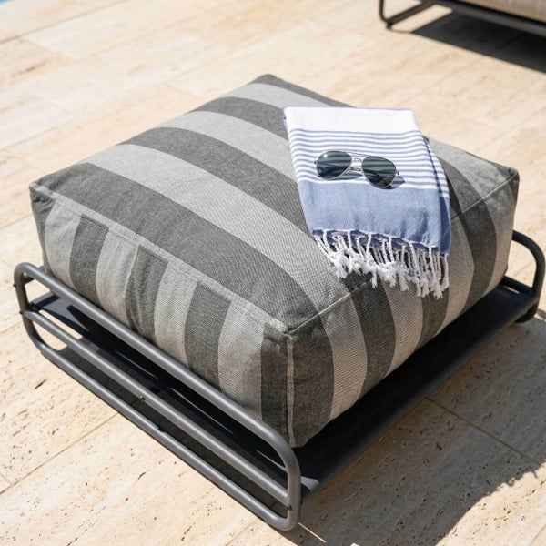 Gestreiftes Outdoor-Sitzkissen auf einem Metallgestell mit Handtuch und Sonnenbrille auf einer Terrasse.