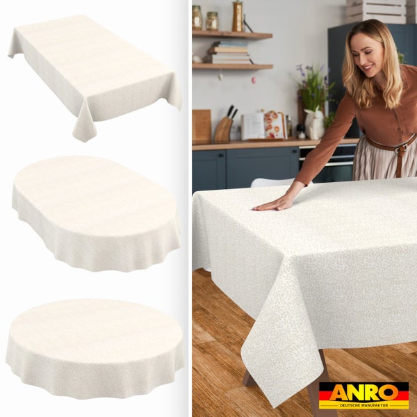 Abwaschbare Tischdecke mit Blattmuster in rechteckiger, ovaler und runder Form. Frau deckt Holztisch in heller Küche mit Tischdecke. ANRO Logo.