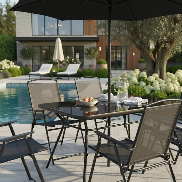 Gartenmöbel-Set bestehend aus einem schwarzen Glastisch, vier Klappstühlen und einem Sonnenschirm auf einer Terrasse am Pool.