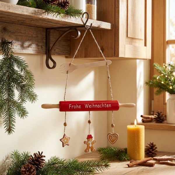 Weihnachtliche Hängedekoration mit Nudelholz und Lebkuchenmotiven in einer gemütlichen Küchenumgebung mit Tannenzweigen und einer Kerze