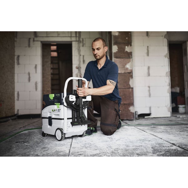 Handwerker kniet auf einer Baustelle neben einem mobilen Festool Absaugmobil und bereitet Zubehör vor.
