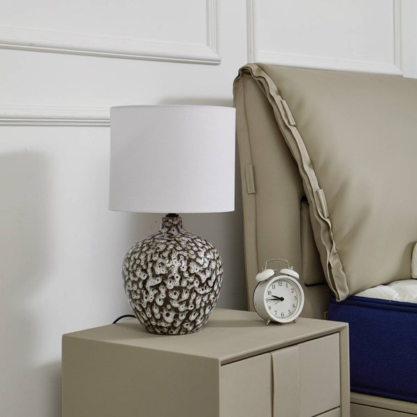 Dekorative Nachttischlampe mit Stoffschirm und Wecker auf einem Nachttisch