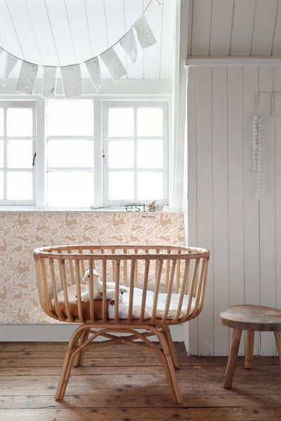 Kinderzimmer mit Babywiege aus Rattan, dekoriert mit Girlande und Hocker