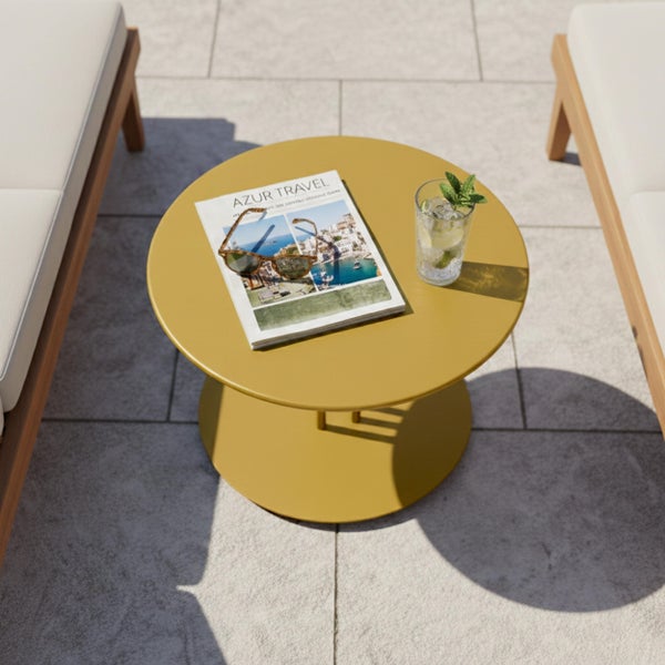 Runder gelber Beistelltisch aus Metall auf einer Terrasse zwischen zwei Gartenliegen mit Magazin, Sonnenbrille und einem Getränk.