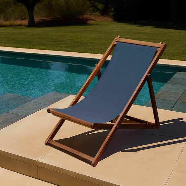 Klappbarer Liegestuhl aus Holz mit blauem Stoffbezug an einem Swimmingpool im Garten.