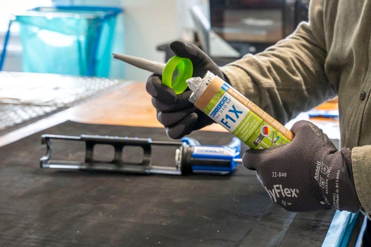 Eine Kartusche Klebstoff wird von einer Person mit Handschuhen geöffnet.