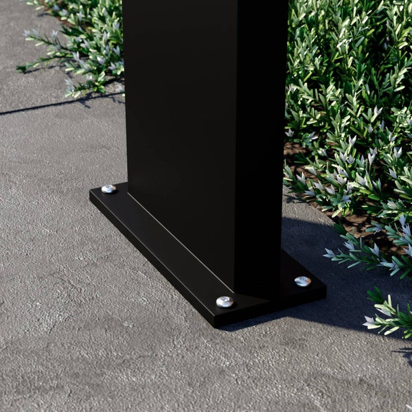Nahaufnahme eines schwarzen, rechteckigen Pfostenträgers, der mit silbernen Schrauben auf einer grauen Fläche neben grünen Pflanzen montiert ist.