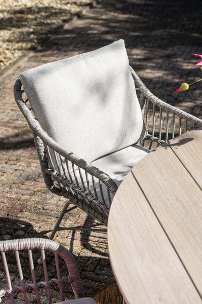 Geflochtener Gartenstuhl mit Sitz- und Rückenkissen an einem runden Holztisch auf einer Terrasse.