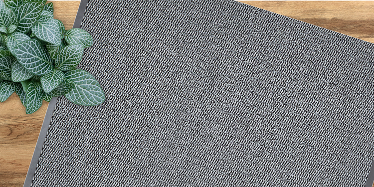 Grau gemusterte Fußmatte mit Pflanze auf Holzboden