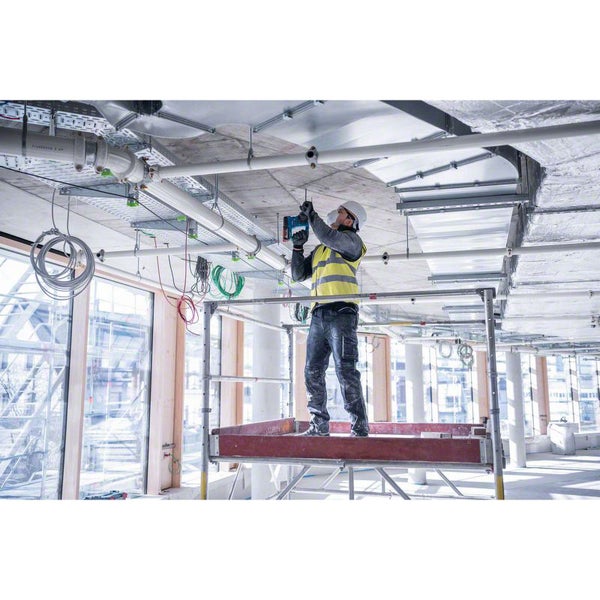 Handwerker auf einem Fahrgerüst bohrt mit einem Akku-Bohrhammer an einer Betondecke auf einer Baustelle.
