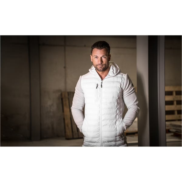 Ein Mann trägt eine weiße Hybridjacke mit Kapuze und gesteppter Vorderseite in einer Werkstattumgebung.