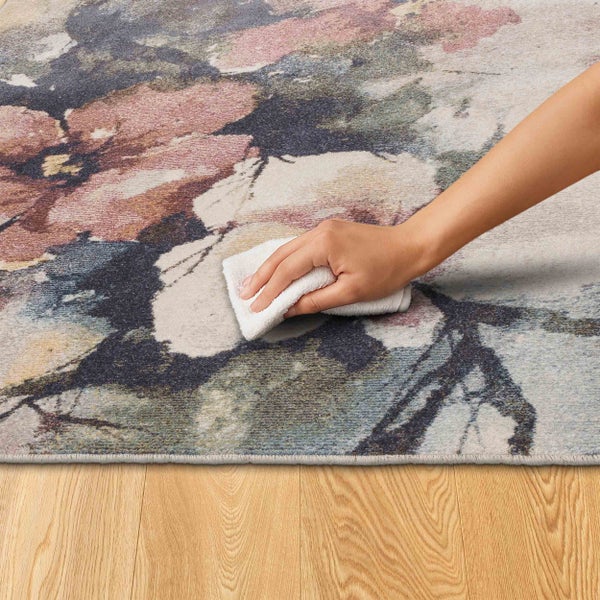 Detailansicht eines gemusterten Teppichs mit einer Hand, die einen Fleck mit einem Tuch entfernt.