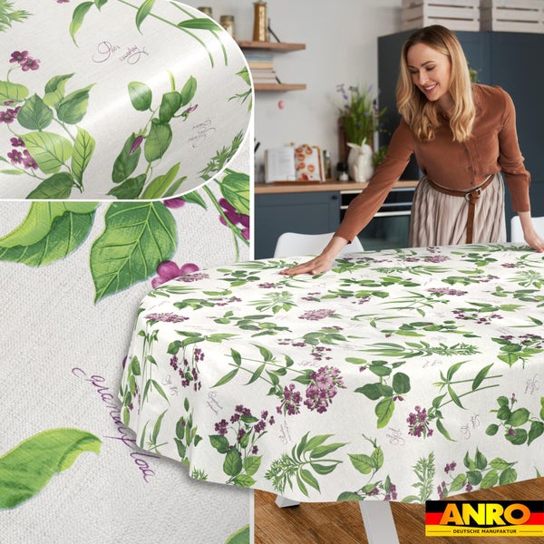 Ovale Wachstuchtischdecke mit grünem Pflanzenmuster und lila Blüten auf einem Küchentisch. ANRO Deutsche Manufaktur Logo.