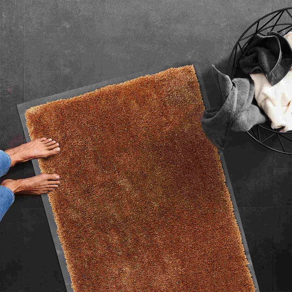 Brauner Badteppich neben einem Handtuchkorb und Füßen auf dunklem Boden