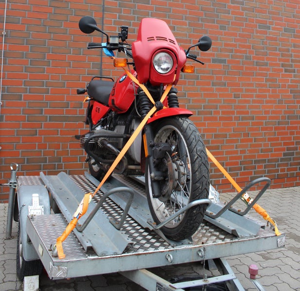 Motorrad auf einem Motorradtransporter sicher mit Spanngurten fixiert vor einer Ziegelwand.