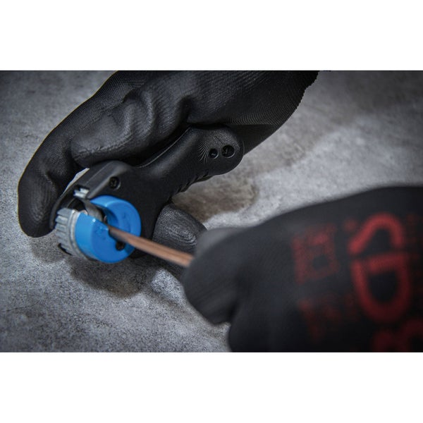 Eine Person mit Handschuhen entfernt die Isolierung eines Kabels mit einem Abmantler und einem Schraubendreher.