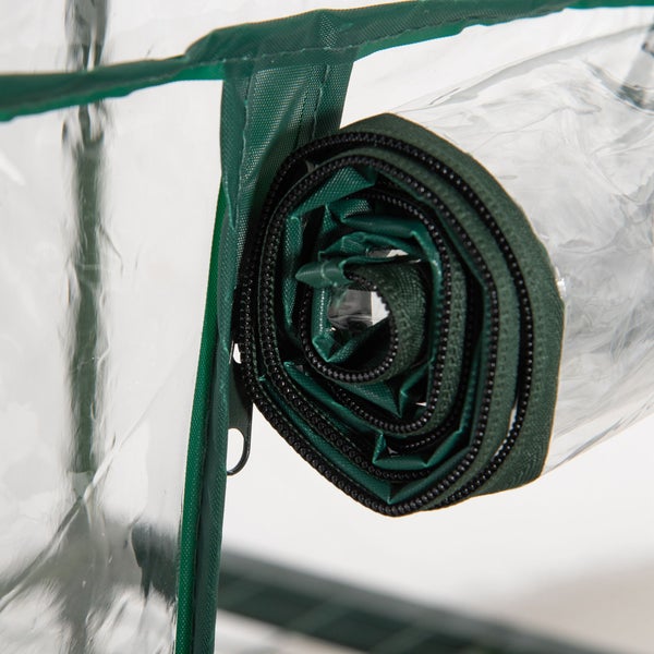 Detailaufnahme einer aufgerollten Tür aus transparenter Folie mit grünem Rand und Reißverschluss eines Foliengewächshauses.