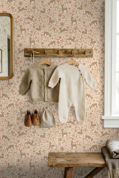 Tapete mit Reh und Blumenmuster in einem Kinderzimmer mit Holzgarderobe und Babykleidung