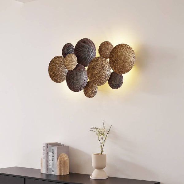 Dekorative Wandleuchte aus überlappenden, strukturierten Metallscheiben mit indirekter Beleuchtung an einer hellen Wand.