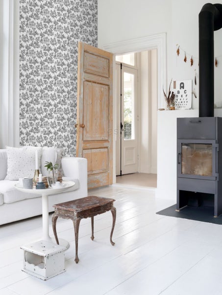 Helles Wohnzimmer mit schwarz-weiß gemusterter Tapete, weißem Sofa, rustikaler Holztür und modernem schwarzen Kaminofen auf weißem Dielenboden.