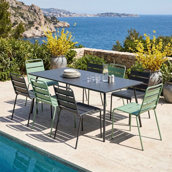 Garten-Essgruppe auf einer Terrasse mit Meerblick, bestehend aus einem anthrazitfarbenen Metalltisch sowie anthrazitfarbenen und grünen Metallstühlen.