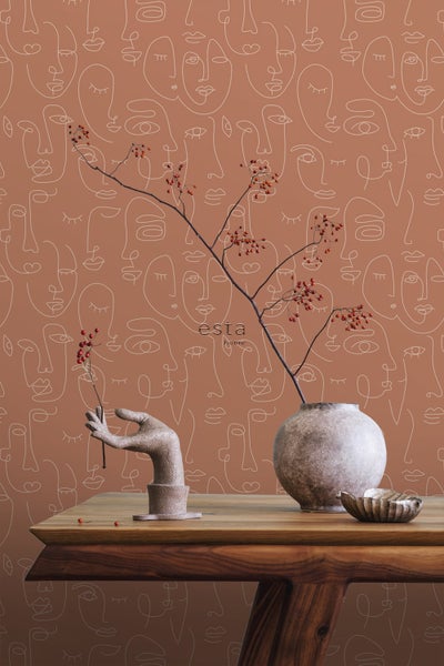 Dekoratives Stillleben auf einem Holztisch vor einer Tapete mit Gesichtsmustern.