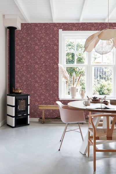 Wohnzimmer mit floral gemusterter Vliestapete, einem Sideboard aus Holz, einem gepolsterten Sessel und einem Fenster mit hellen Vorhängen.