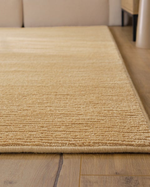 Beige gerippter Teppich mit strukturierter Oberfläche auf einem Holzboden.