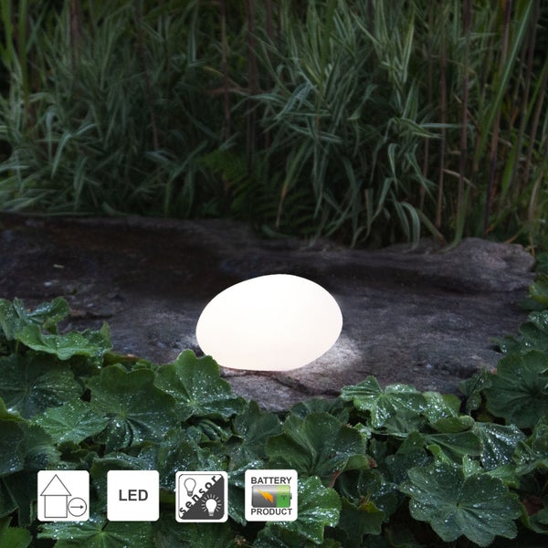 Leuchtende Gartenleuchte in Ei-Form auf Stein und Grünpflanzen