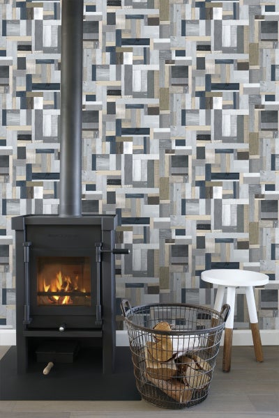 Wohnzimmer mit Kaminofen, Holzkorb und Hocker vor einer Wand mit Holzpaneel-Tapete.