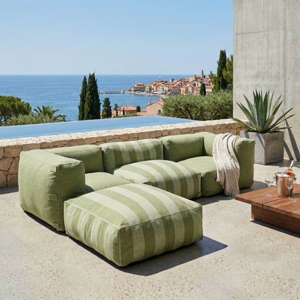 Modernes modulares Outdoor-Sofa mit grünem Streifenmuster, Hocker und Holztisch auf einer hellen Terrasse mit Pool und Meerblick.