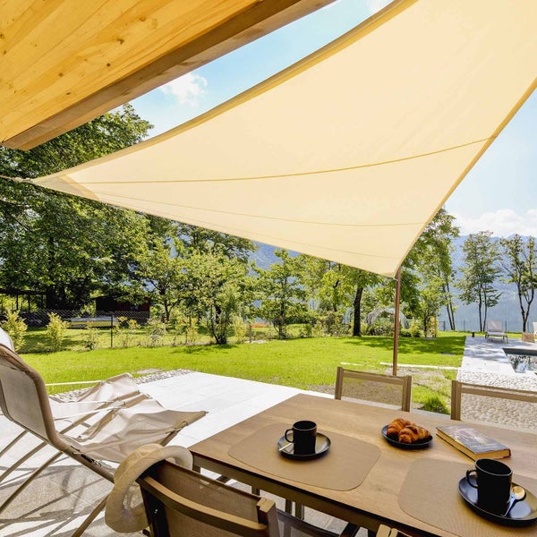 Sonnensegel über einer Terrasse mit Holztisch und Stühlen gespannt, mit Blick auf einen weitläufigen Garten.