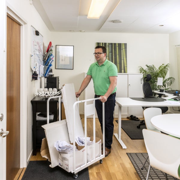 Mann schiebt einen Rollwagen mit Kartons und Papier in einem Büro.