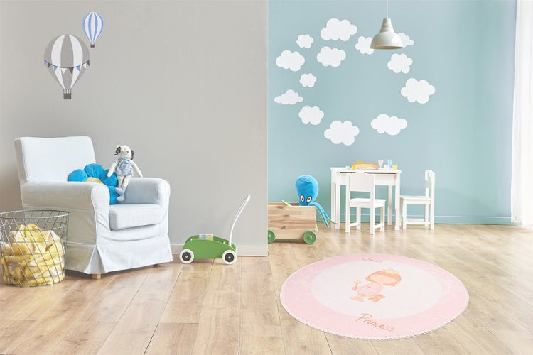 Ein hell eingerichtetes Kinderzimmer mit einem runden Kinderteppich, einem Sessel, einem Kindertisch und Wandaufklebern mit Wolken und Heißluftballon.