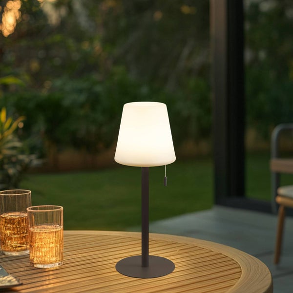 LED-Außen-Tischleuchte mit warmweißem Licht auf einem runden Holztisch im Garten.