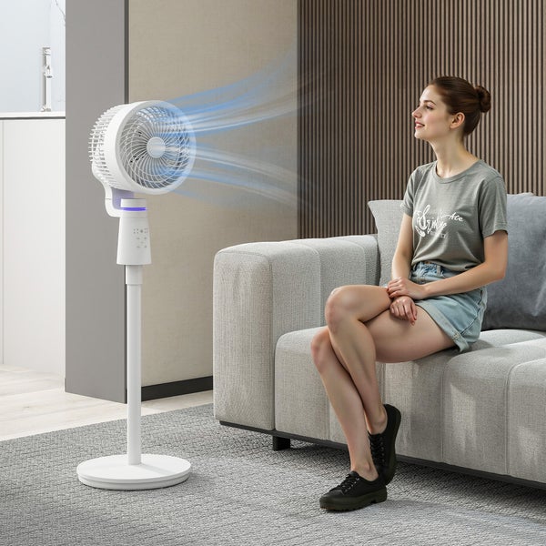 Moderner weißer Standventilator, der Luft in Richtung einer Frau auf einem Sofa in einem hellen, organisierten Wohnzimmer bläst.