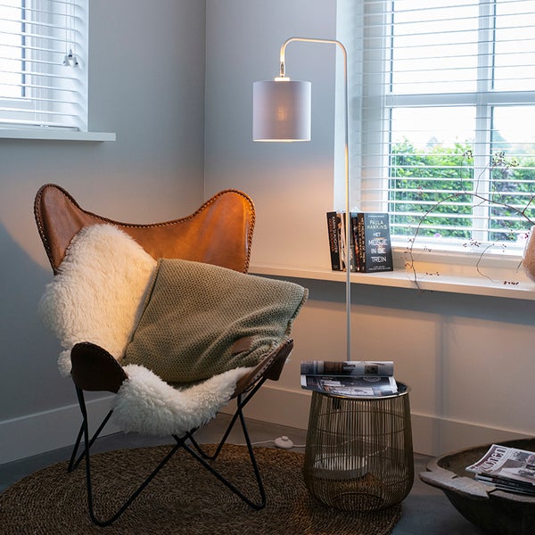 Moderne Leseecke mit einem braunen Butterfly Sessel aus Leder, einer weißen Bogen Stehleuchte, einem grünen Kissen und einem runden Juteteppich.