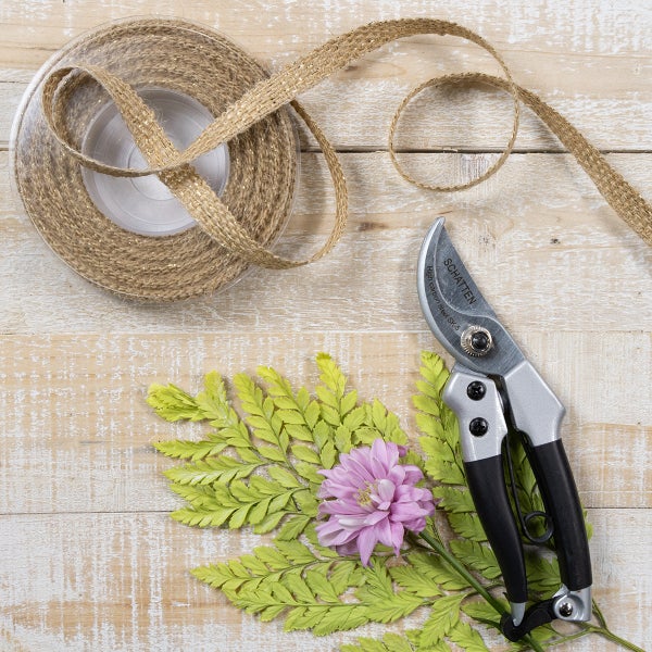 Gartenschere mit Schatten Logo, Juteband, Blume und Blättern auf einer Holzoberfläche.