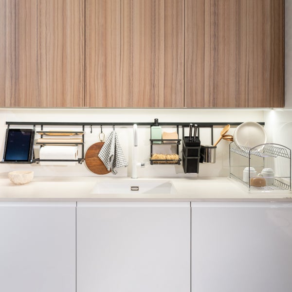 Helle, moderne Küche mit Holzschränken, weißer Spüle und einem schwarzen Relingsystem für Küchenutensilien wie Messerblock und Tablethalter.