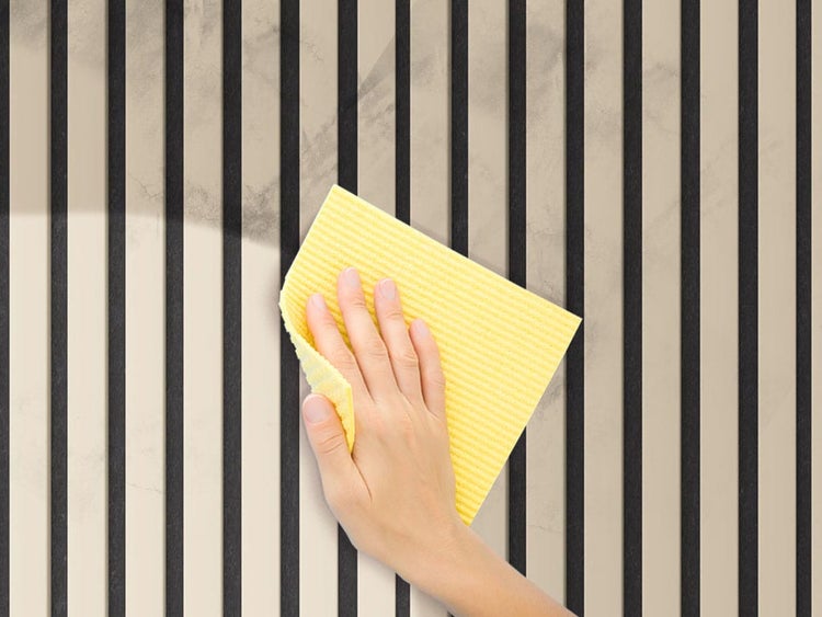 Eine Hand reinigt eine Lamellenwand mit einem Reinigungstuch.