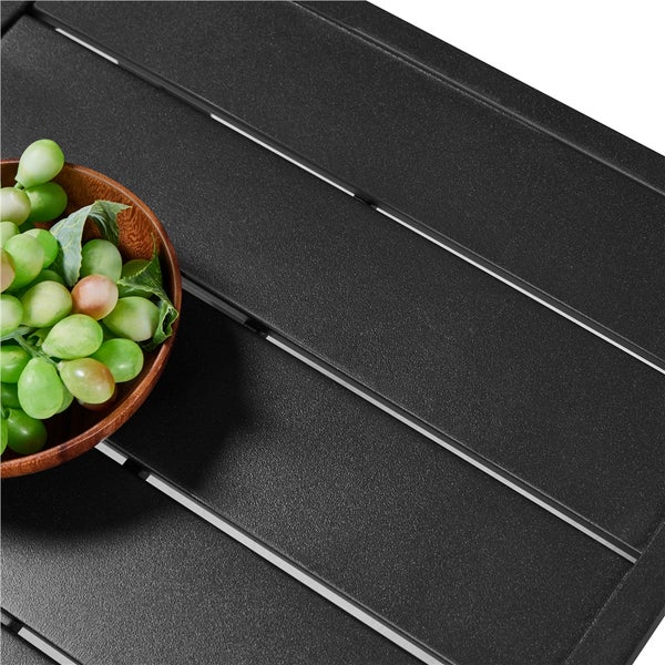 Detailansicht einer strukturierten Tischoberfläche aus Aluminium-Lamellen mit einer Holzschale voller Weintrauben.