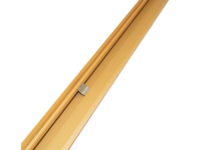 Goldfarbenes Metallprofil mit gerillter Oberfläche und einem kleinen silberfarbenen Clip.