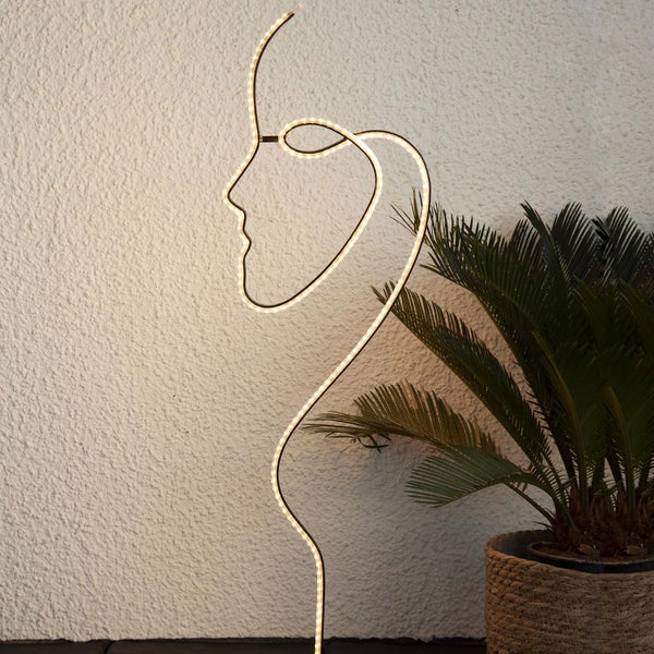 Dekorative LED-Stehleuchte in Form eines Frauengesichts neben einer Zimmerpflanze