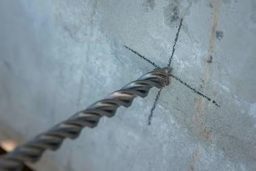 Betonbohrer angesetzt an einer Markierung auf einer Betonwand.