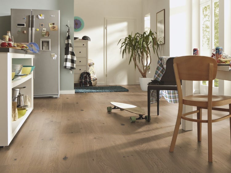 Moderner, heller Wohnbereich mit hellem Holzboden in Eichenoptik, mit Küchentheke, Kühlschrank, Essbereich und einer großen Pflanze.