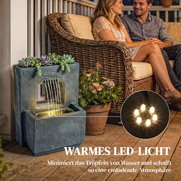 Grauer rechteckiger Gartenbrunnen mit integriertem Pflanzgefäß für Sukkulenten, warmem LED-Licht und mehreren Wasserfällen auf einer Holzterrasse.