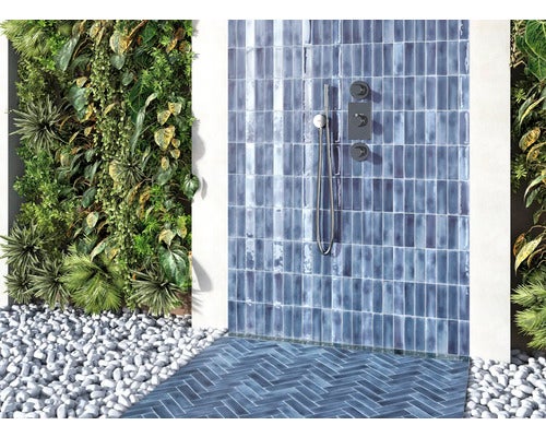 Badezimmerbereich mit blauen Fliesen, Dusche, Pflanzenwand und Kieselsteinen