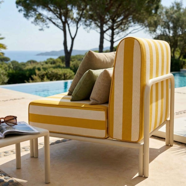 Moderner Garten-Sessel mit gelb-weiß gestreiften Polstern und Metallgestell auf einer Terrasse am Pool mit Meerblick und dekorativen Kissen.