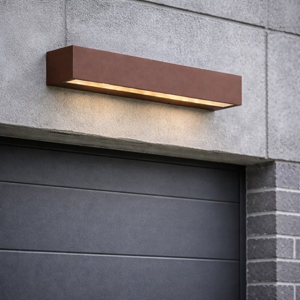 Rechteckige Außenwandleuchte mit Lichtaustritt nach unten, montiert an einer Betonwand über einem Garagentor.