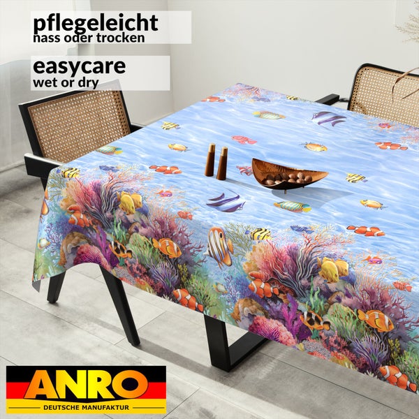 ANRO Deutsche Manufaktur Logo. Pflegeleichte Tischdecke mit bunten Fischen und Korallen auf einem Esstisch in einem hellen, modernen Raum.